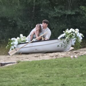 Bride and groom in a flower-decorated canoe on the lake at Caribou Bay Retreat during sunset, with green trees reflecting in the water.