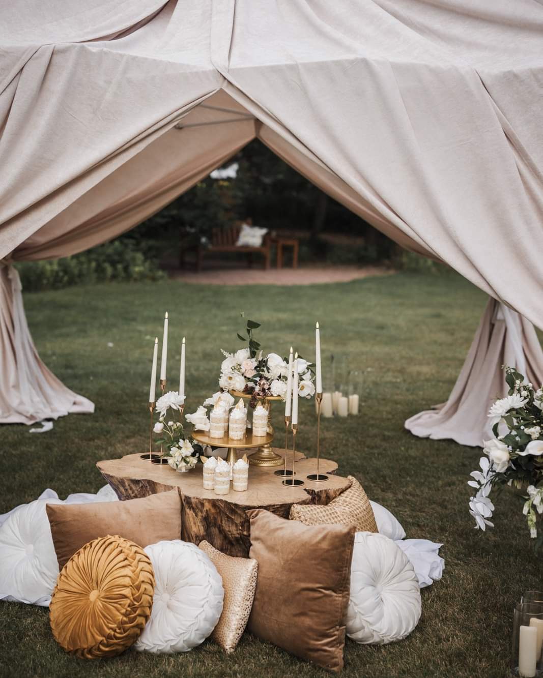 Shaded garden lounge setup with neutral draping, white and gold pillows, rustic low table, and candlelight at Caribou Bay Retreat.