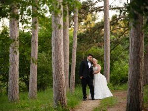 Bride and groom walking together on a wooded path surrounded by tall pine trees at Caribou Bay Retreat in Central Wisconsin