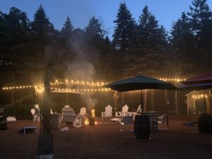 Fire pit surrounded by Adirondack chairs, string lights, and tall pine trees at Caribou Bay Retreat in Central Wisconsin