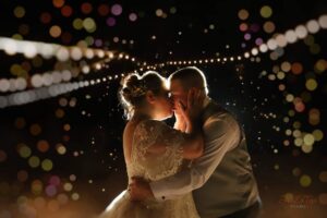 Bride and groom share a tender kiss under glowing string lights, surrounded by a dreamy bokeh effect at Caribou Bay Retreat.