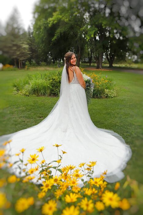 Bride in a flowing white gown standing in a garden at Caribou Bay Retreat, with yellow flowers in the foreground and lush trees in the background.