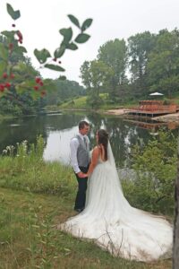 Bride and groom holding hands by a quiet lake at Caribou Bay Retreat, with a wooden lakeside deck in the background.