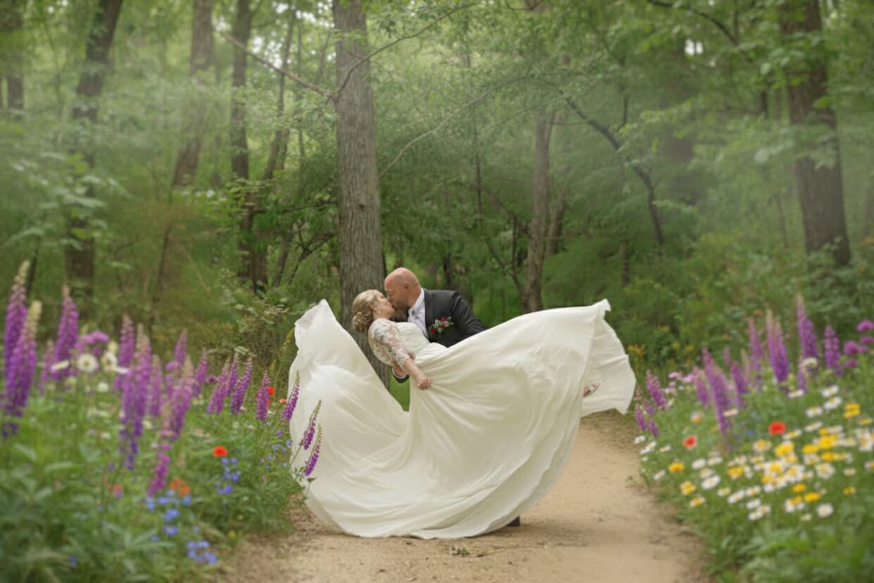 Groom dipping bride for a kiss on a woodland path surrounded by wildflowers at Caribou Bay Retreat.