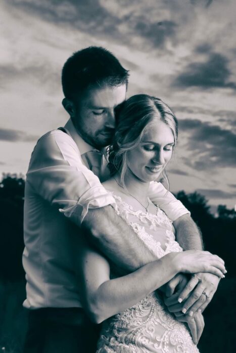 Bride and groom embrace tenderly at sunset, captured in a romantic black and white wedding portrait.