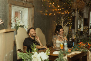 Central Wisconsin wedding venue near Appleton at Caribou Bay Retreat – bride and groom laughing together at the sweetheart table surrounded by twinkle lights and rustic décor inside the Event Center.