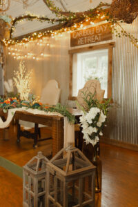 Central Wisconsin wedding venue near Oshkosh at Caribou Bay Retreat – sweetheart table with rustic wood accents, floral greenery, and twinkle lights under a grapevine canopy inside the Event Center.