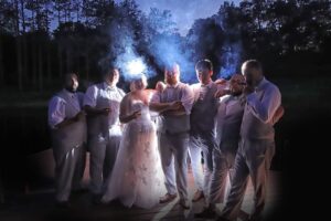 Central Wisconsin wedding venue near Wisconsin Dells at Caribou Bay Retreat – bride and groomsmen sharing cigars on the lakeside deck under the night sky with glowing smoke and dramatic lighting.
