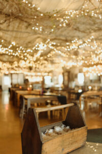 Central Wisconsin wedding venue near Portage at Caribou Bay Retreat – rustic event center with wooden tables, twinkle-light grapevine ceiling, and wooden box of wedding favors.