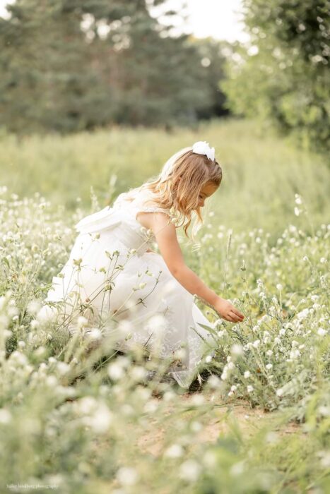 Central Wisconsin wedding venue near Stevens Point at Caribou Bay Retreat – young flower girl in a white dress picking wildflowers in a sunlit meadow.