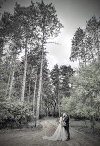 Central Wisconsin wedding venue near Stevens Point at Caribou Bay Retreat – bride and groom standing on a rustic forest path surrounded by towering pines, embracing beneath the canopy.
