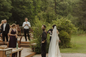 Central Wisconsin wedding venue near Wisconsin Dells at Caribou Bay Retreat – bride and groom sharing a quiet candid moment on the wooden deck as guests mingle after an outdoor ceremony