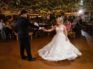 Central Wisconsin wedding venue near Oshkosh at Caribou Bay Retreat – bride and groom sharing their first dance beneath twinkle lights in the rustic indoor reception space