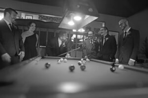 Central Wisconsin wedding venue near Wisconsin Dells at Caribou Bay Retreat – wedding party laughing and playing pool together inside the lodge during a relaxed wedding weekend