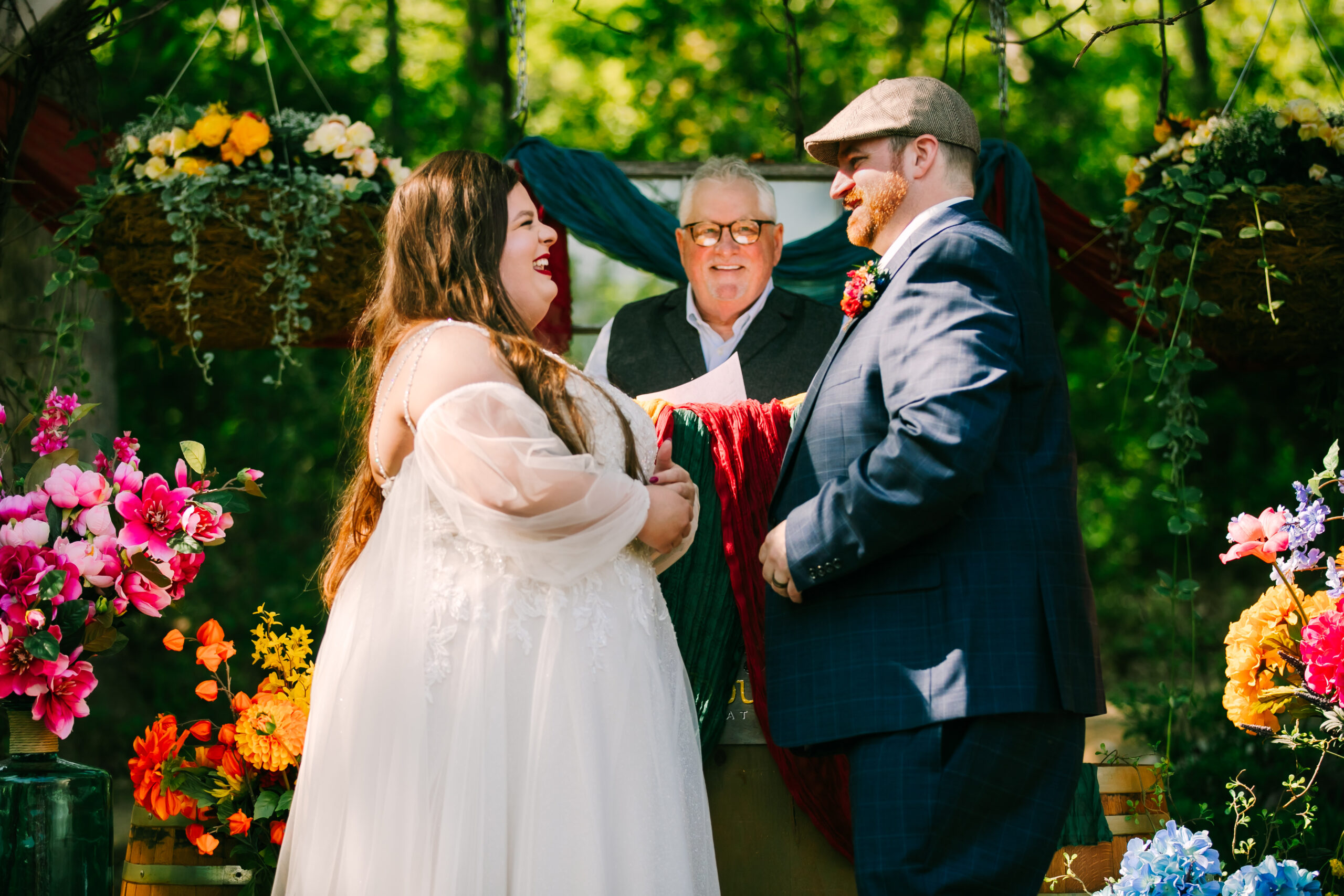 Central Wisconsin wedding venue near Stevens Point at Caribou Bay Retreat – bride and groom smiling and holding hands during an intimate outdoor chapel ceremony surrounded by colorful flowers and woodland greenery.