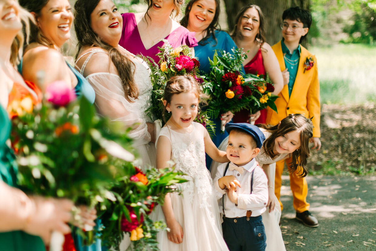 Central Wisconsin wedding venue near Wisconsin Dells at Caribou Bay Retreat – joyful bride surrounded by bridesmaids and children in colorful attire sharing a candid outdoor moment during a wedding celebration.