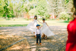 Central Wisconsin wedding venue near Oshkosh at Caribou Bay Retreat – flower girls in soft dresses and a young ring bearer walking along a sunlit tree-lined path during a joyful wedding day moment.