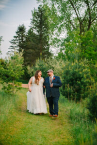 Central Wisconsin wedding venue near Portage at Caribou Bay Retreat – bride and groom walking together along a peaceful green woodland path surrounded by pine trees.