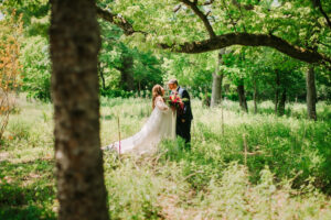 Central Wisconsin wedding venue near Wisconsin Dells at Caribou Bay Retreat – bride and groom sharing a romantic moment in a sunlit wooded setting with lush greenery