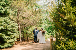 Central Wisconsin wedding venue near Appleton at Caribou Bay Retreat – bride and groom walking hand in hand along a wooded path surrounded by pine trees and natural greenery