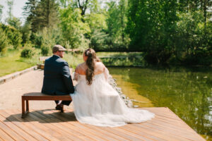 Central Wisconsin wedding venue near Stevens Point at Caribou Bay Retreat – bride and groom sitting together on a wooden deck overlooking a peaceful lake surrounded by lush greenery
