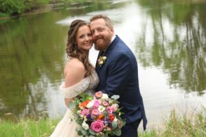 Central Wisconsin wedding venue near Appleton at Caribou Bay Retreat – bride and groom embracing by the lake with a colorful bouquet and peaceful waterfront backdrop