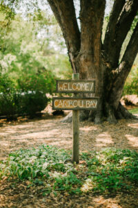 Central Wisconsin wedding venue near Oshkosh at Caribou Bay Retreat – rustic wooden welcome sign surrounded by greenery and mature trees at the entrance